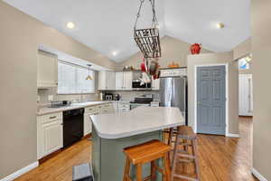 Kitchen featuring a breakfast bar area, light countertops, white cabinetry, vaulted ceiling, and appliances with stainless steel finishes