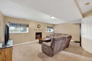 Living room with light colored carpet, plenty of natural light, a warm lit fireplace, and a textured ceiling