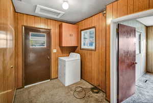 Laundry area featuring washer / clothes dryer, attic access, light colored carpet, wooden walls, and cabinet space