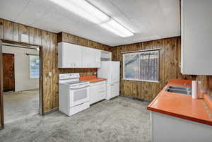 Kitchen with wood walls, white appliances, white cabinets, light colored carpet, and light countertops
