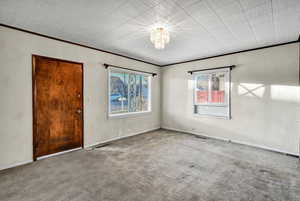Empty room featuring ornamental molding, carpet flooring, and a chandelier