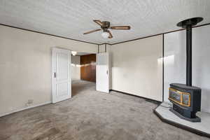 Unfurnished living room featuring a wood stove, carpet, and a ceiling fan