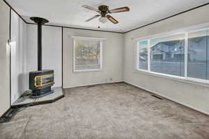 Unfurnished living room with a wood stove, carpet flooring, and ceiling fan