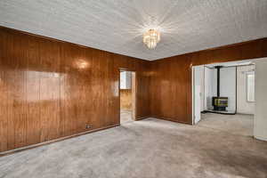 Carpeted empty room with a wood stove, wooden walls, and a chandelier