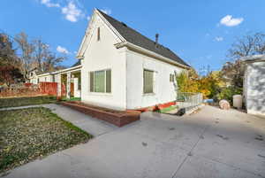 View of side of property with a shingled roof, stucco siding, and covered porch