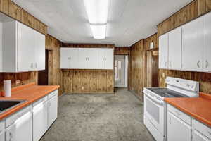 Kitchen featuring white electric range oven, wood walls, light countertops, light carpet, and white cabinetry