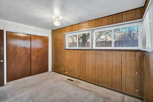 Unfurnished bedroom featuring wooden walls, carpet flooring, and a closet