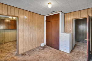 Unfurnished bedroom featuring carpet, wood walls, and a closet