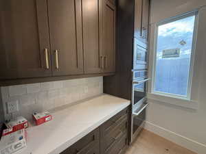 Kitchen featuring tasteful backsplash, dark brown cabinetry, light wood-style flooring, appliances with stainless steel finishes, and light stone counters