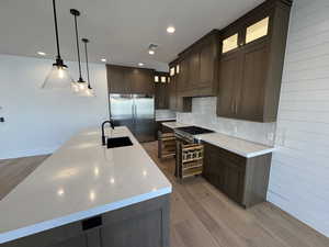 Kitchen featuring dark wood-style flooring, dark brown cabinets, decorative light fixtures, decorative backsplash, and built in refrigerator