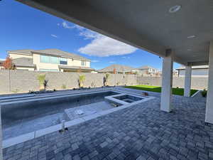 Fenced backyard with a patio, a residential view, and a pool with connected hot tub
