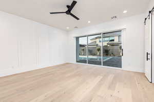 Unfurnished room with a barn door, light wood finished floors, a decorative wall, a ceiling fan, and recessed lighting