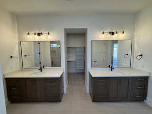 Full bath with a walk in closet, two vanities, light tile patterned floors, and a stall shower