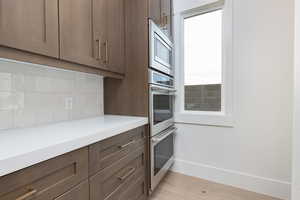Kitchen with appliances with stainless steel finishes, light wood-type flooring, decorative backsplash, and light stone countertops