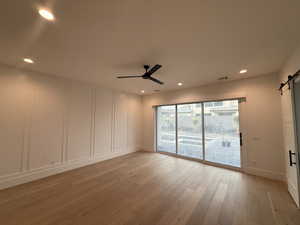 Spare room featuring a barn door, light wood-style flooring, ceiling fan, recessed lighting, and a decorative wall