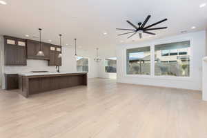 Kitchen featuring glass insert cabinets, dark brown cabinetry, decorative light fixtures, a large island, and open floor plan