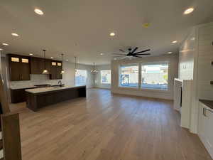 Kitchen featuring glass insert cabinets, dark brown cabinets, open floor plan, a chandelier, and light wood-style flooring