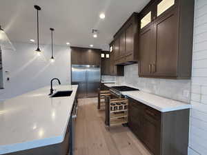 Kitchen with dark brown cabinetry, glass insert cabinets, pendant lighting, appliances with stainless steel finishes, and light wood-style flooring