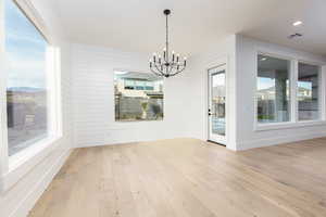 Unfurnished dining area featuring a chandelier, light wood-style flooring, wooden walls, and recessed lighting