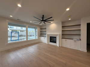 Unfurnished living room featuring light wood finished floors, recessed lighting, a large fireplace, built in shelves, and a ceiling fan