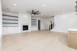Unfurnished living room with a fireplace, light wood-style floors, stairs, recessed lighting, and a ceiling fan