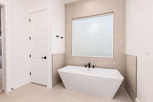 Full bathroom with tile walls, a freestanding tub, and light tile patterned floors