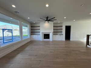 Unfurnished living room with built in features, a fireplace, ceiling fan, light wood-type flooring, and recessed lighting