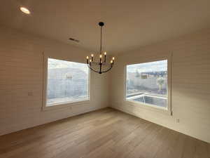 Unfurnished dining area featuring wood walls, hardwood / wood-style floors, a chandelier, healthy amount of natural light, and recessed lighting