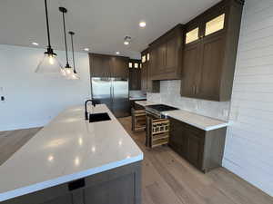 Kitchen featuring dark brown cabinets, dark wood-style floors, decorative light fixtures, stainless steel built in refrigerator, and a center island with sink