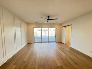Empty room with a barn door, light wood-type flooring, ceiling fan, and recessed lighting