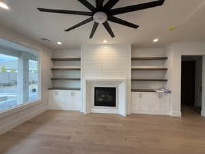 Unfurnished living room with light wood-style flooring, recessed lighting, a glass covered fireplace, built in shelves, and ceiling fan