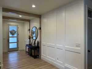 Hall with light wood-type flooring, a decorative wall, beam ceiling, and recessed lighting