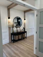 Hall featuring light wood finished floors, beam ceiling, and a decorative wall