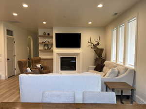 Living area with recessed lighting, a glass covered fireplace, arched walkways, wood finished floors, and built in features