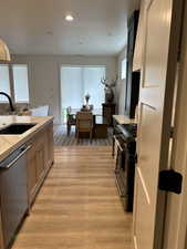 Kitchen featuring range with two ovens, stainless steel dishwasher, light wood finished floors, recessed lighting, and light brown cabinetry