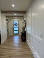 Corridor with beamed ceiling, light wood-style floors, recessed lighting, and a decorative wall