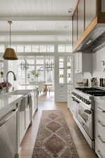 Kitchen featuring appliances with stainless steel finishes, range hood, beamed ceiling, white cabinetry, and light stone countertops