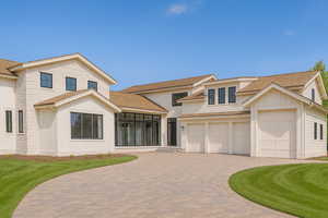 View of front of home featuring roof with shingles, decorative driveway, board and batten siding, and a front lawn