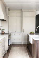 Kitchen with light stone countertops, high end stainless steel range oven, premium range hood, dark wood-style floors, and ornamental molding