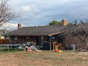Rear view of property with a trampoline, a chimney, brick siding, and a shingled roof