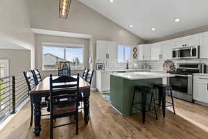 Kitchen featuring green cabinets, stainless steel appliances, white cabinets, tasteful backsplash, and high vaulted ceiling