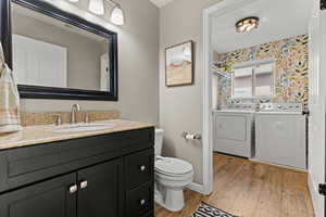Bathroom with light wood-style flooring, washing machine and dryer, vanity, and wallpapered walls