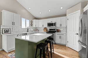 Kitchen with appliances with stainless steel finishes, tasteful backsplash, lofted ceiling, white cabinetry, and recessed lighting