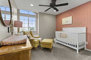 Carpeted bedroom with a crib, ceiling fan, wood walls, and recessed lighting