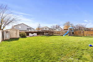 Fenced backyard featuring a storage shed, a residential view, and a playground