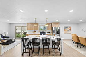 Kitchen featuring a kitchen island, a breakfast bar area, pendant lighting, light wood-type flooring, and open floor plan