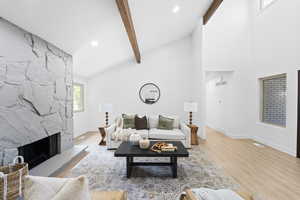 Living area with plenty of natural light, wood finished floors, beam ceiling, a stone fireplace, and high vaulted ceiling