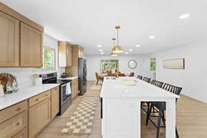 Kitchen featuring a kitchen bar, appliances with stainless steel finishes, light stone countertops, hanging light fixtures, and a kitchen island with sink