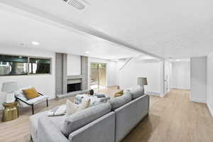 Living room featuring light wood finished floors, a textured ceiling, stairway, a brick fireplace, and recessed lighting