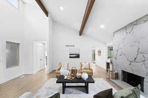 Living area featuring beamed ceiling, a stone fireplace, high vaulted ceiling, and wood finished floors